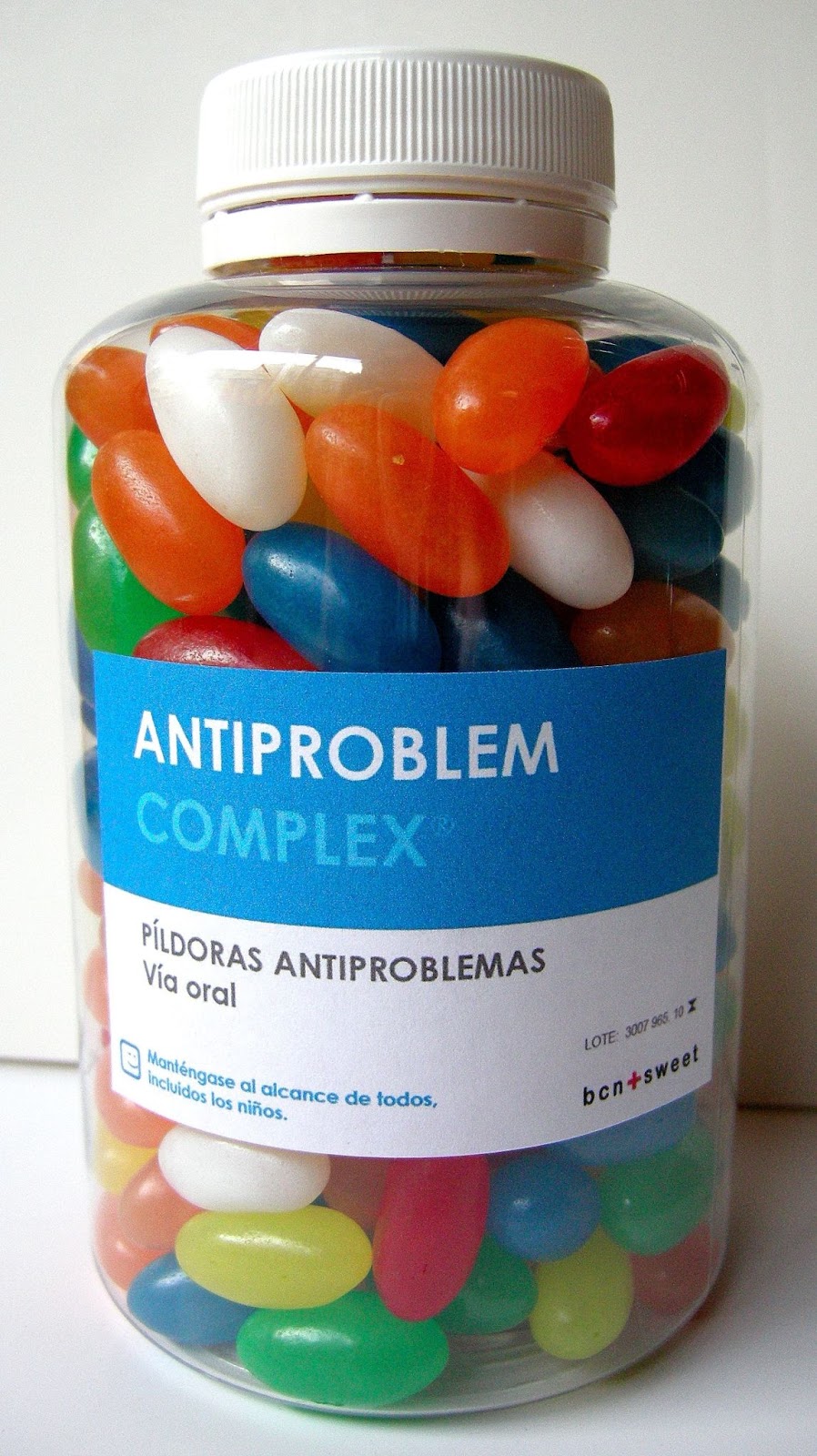 A imagem é uma embalagem de pílulas de remédio cheia de balas de jujuba. A embalagem diz "complexo antiproblemas. Pílulas antiproblemas. via oral. Mantenha ao alcance de todos, inclusive crianças"